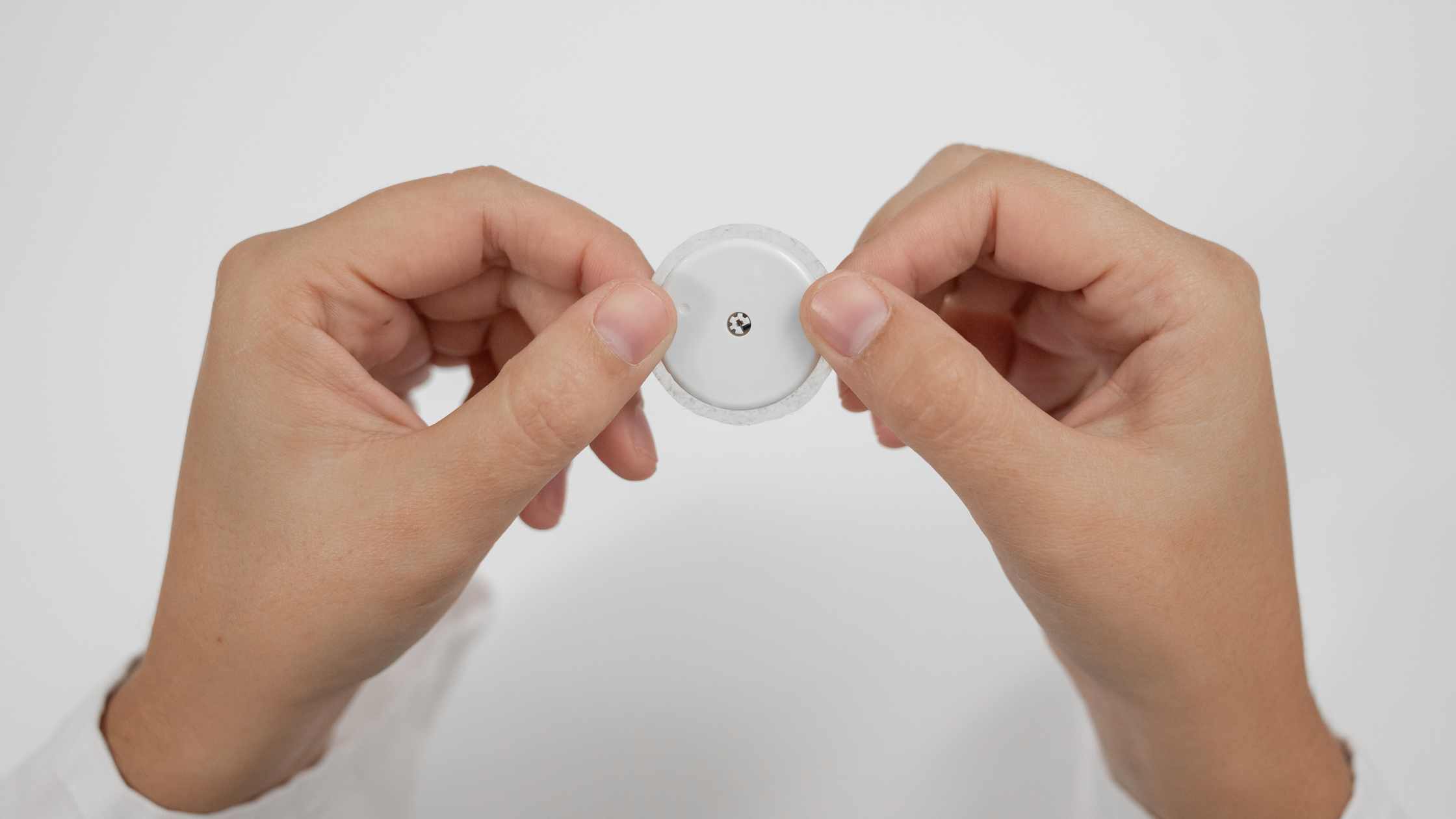 Two hands holding a werable microneedle device.