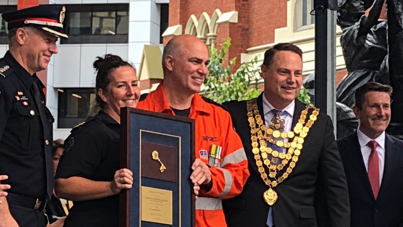 Emergency services volunteers holding the framed Key to the City of Brisbane on stage with the Lord Mayor and fire service leaders.