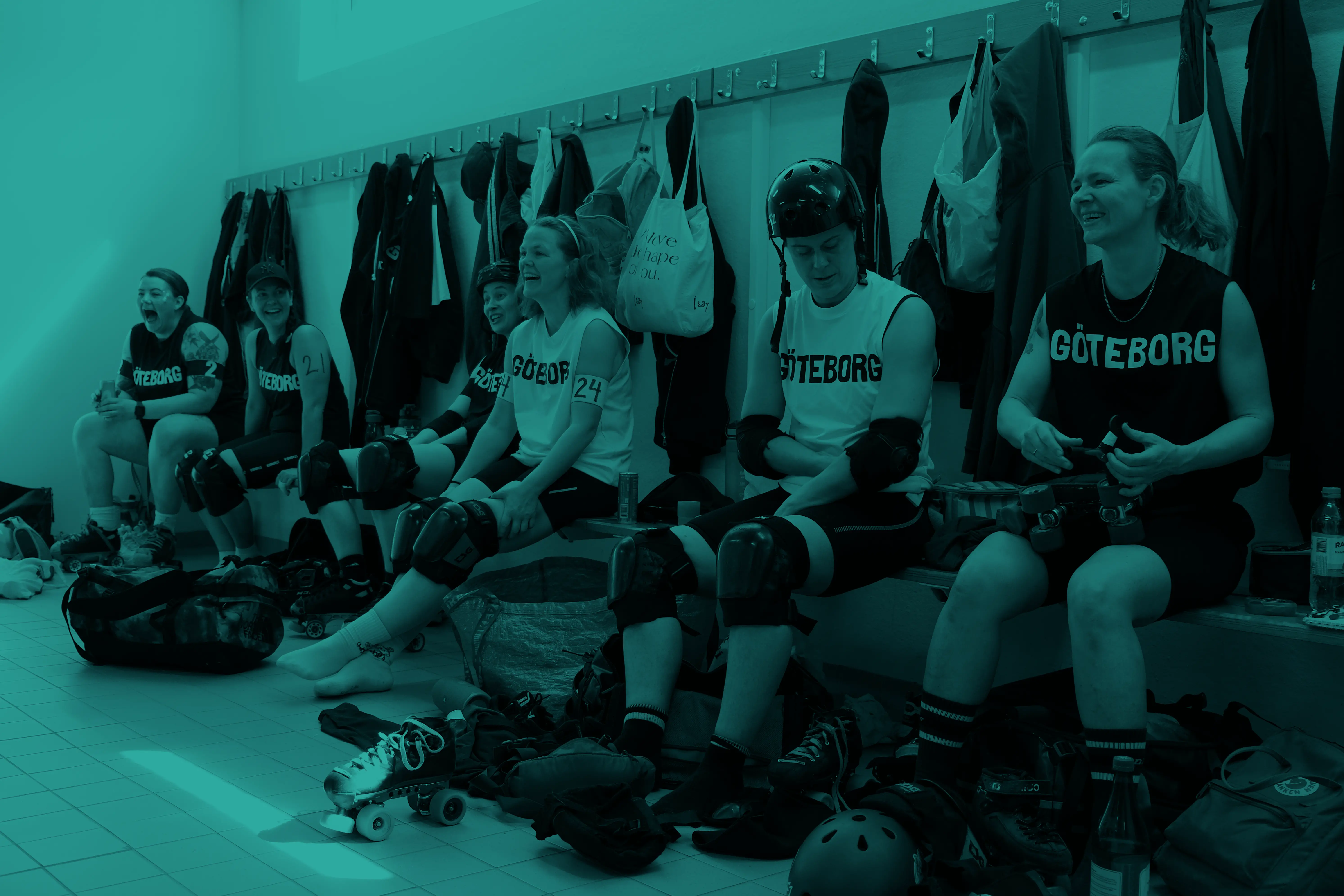 A group of roller derby players putting on roller derby gear while laughing in a changing room.