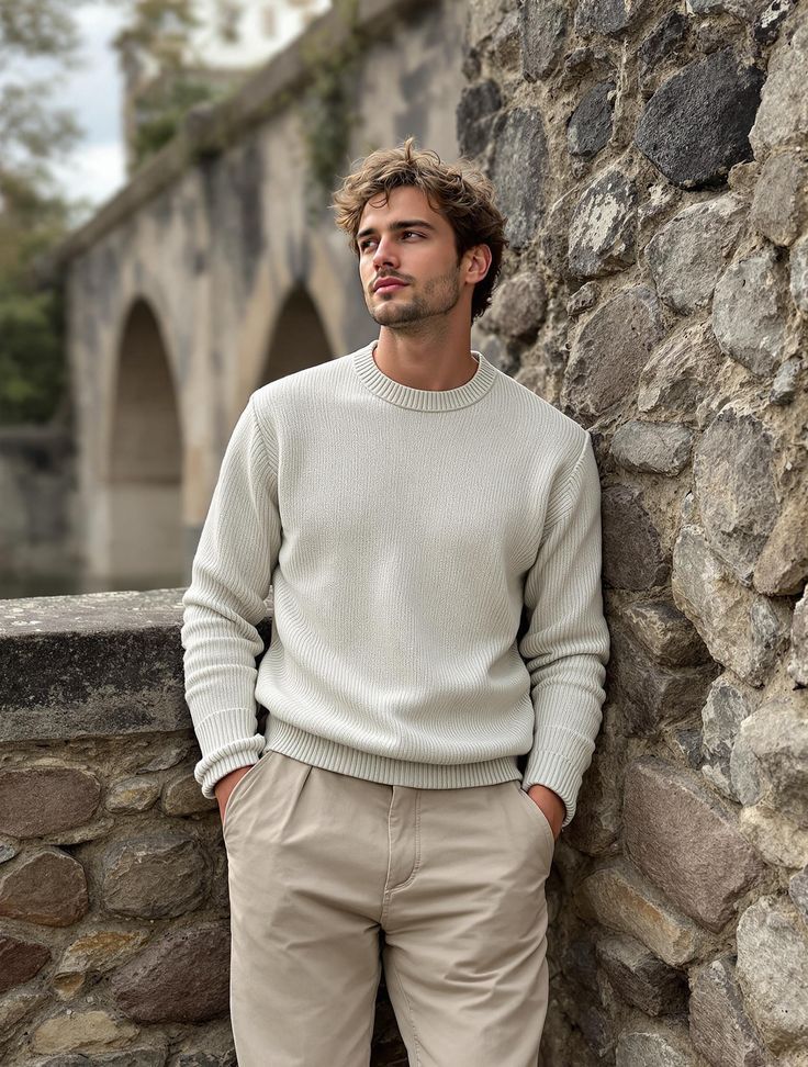 Young woman with curly hair wearing a white shirt and pants sitting on a couch in warm, dim lighting.
