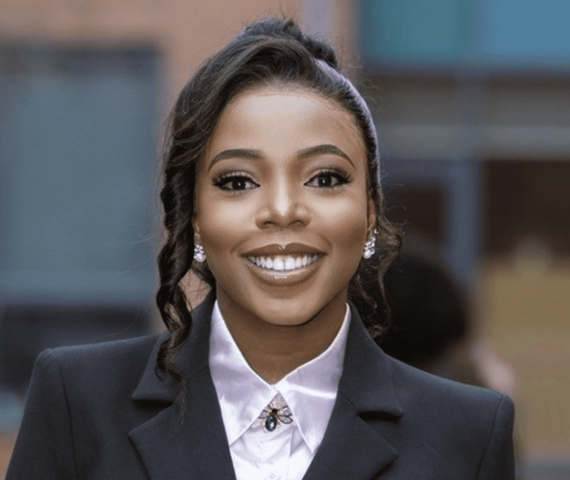 Person wearing a textured purple top with long hair pulled to one side, shown from the shoulders up.