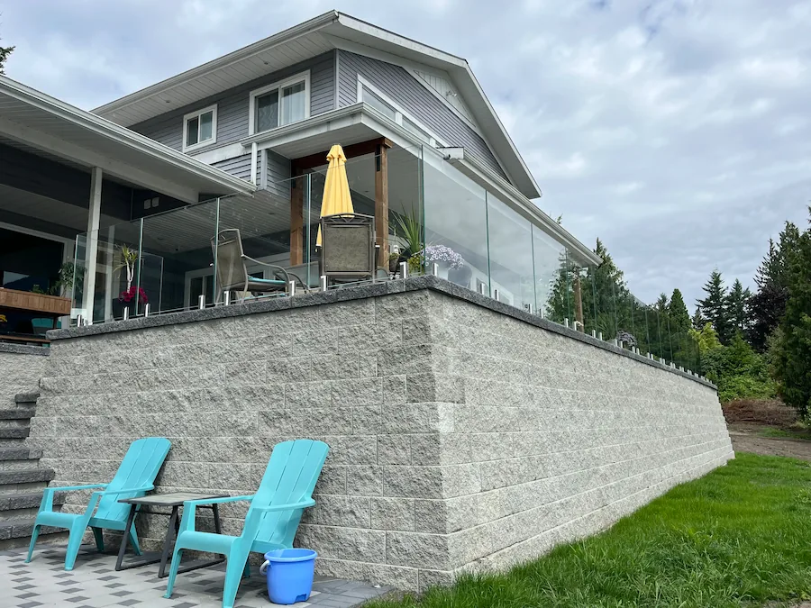 Elevated patio with frameless glass railings installed along a retaining wall, providing safety and unobstructed yard and landscape views.