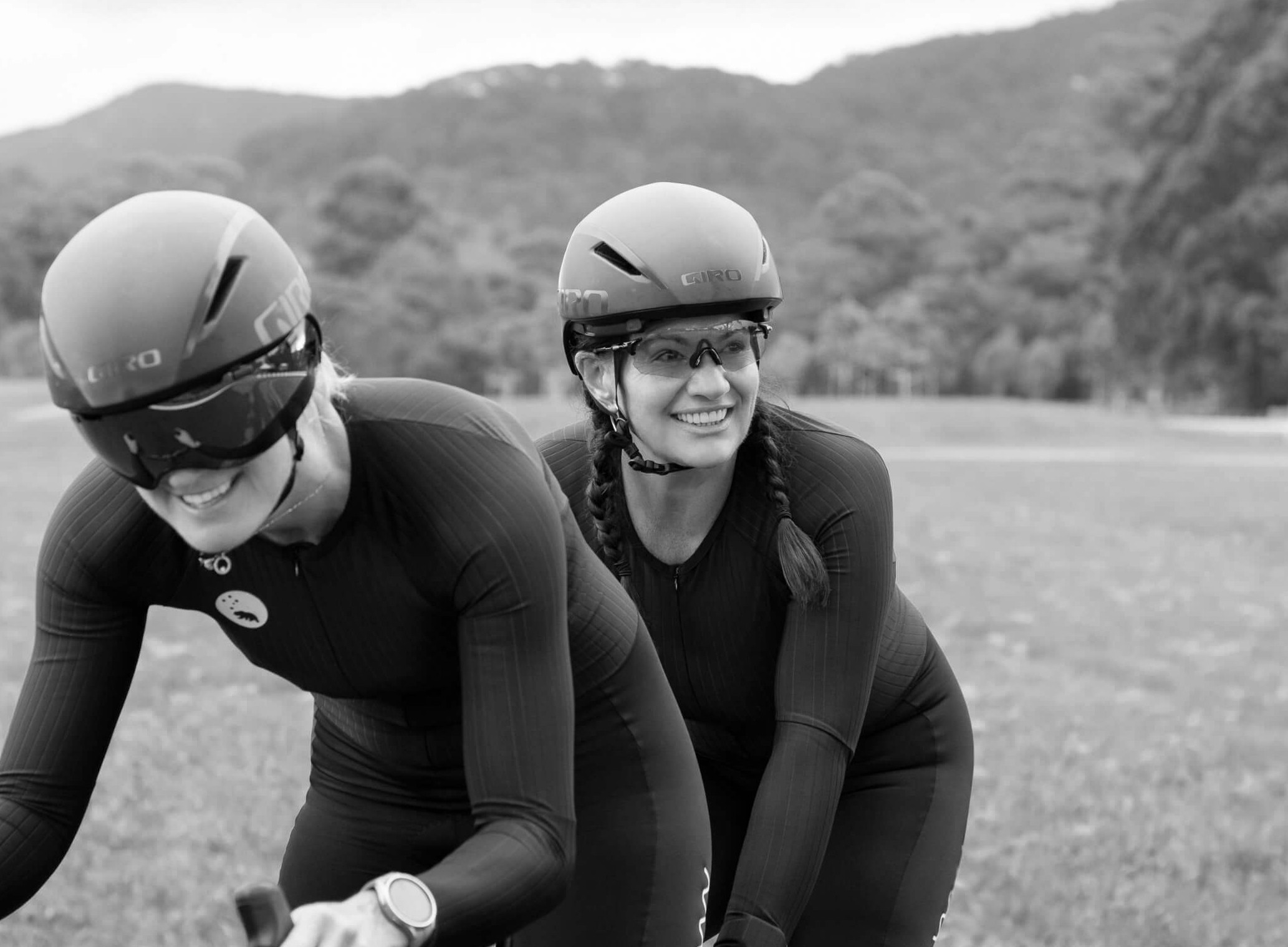 Lily on her tandem riding with pilot, Jay, they are wearing their black cycling kit with black time trial helmets.