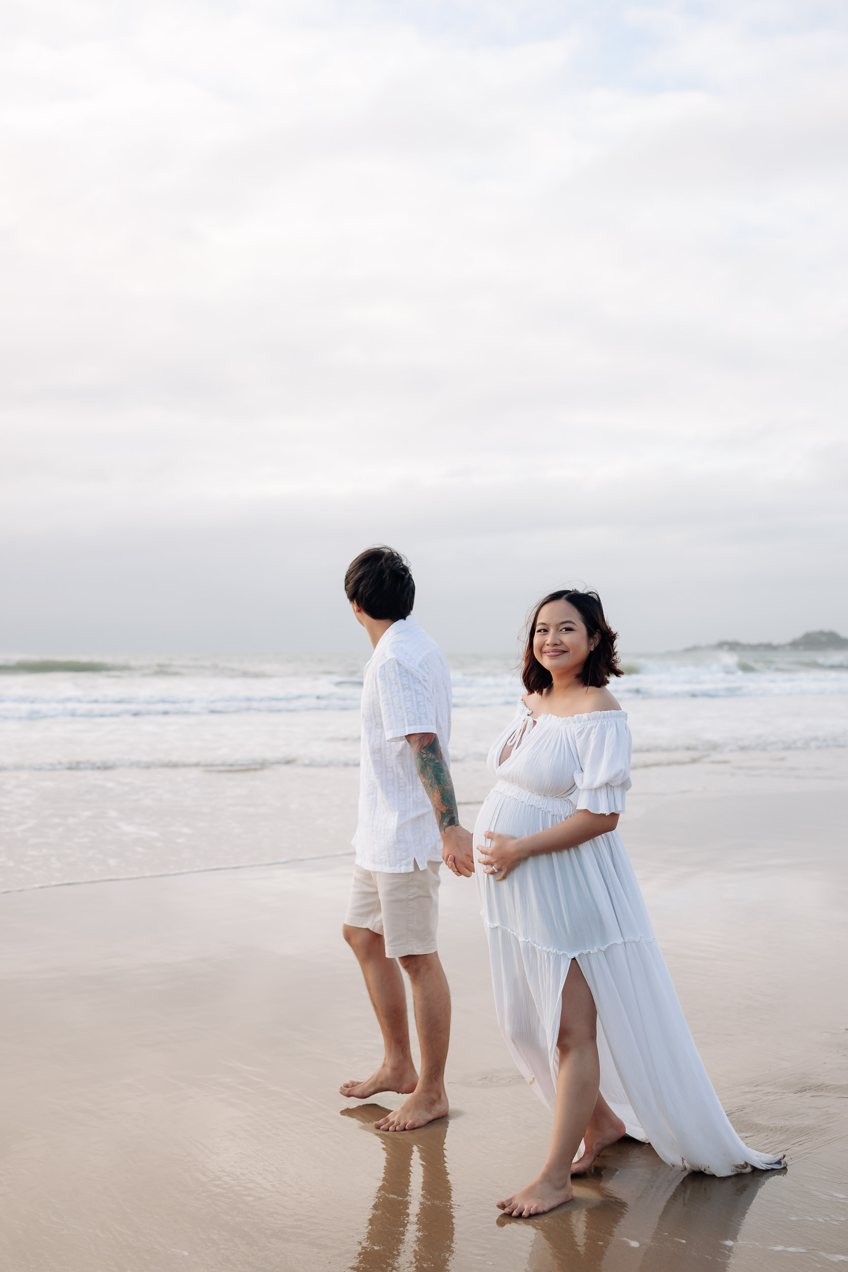 Pregnant couple holding hands walking along the beach