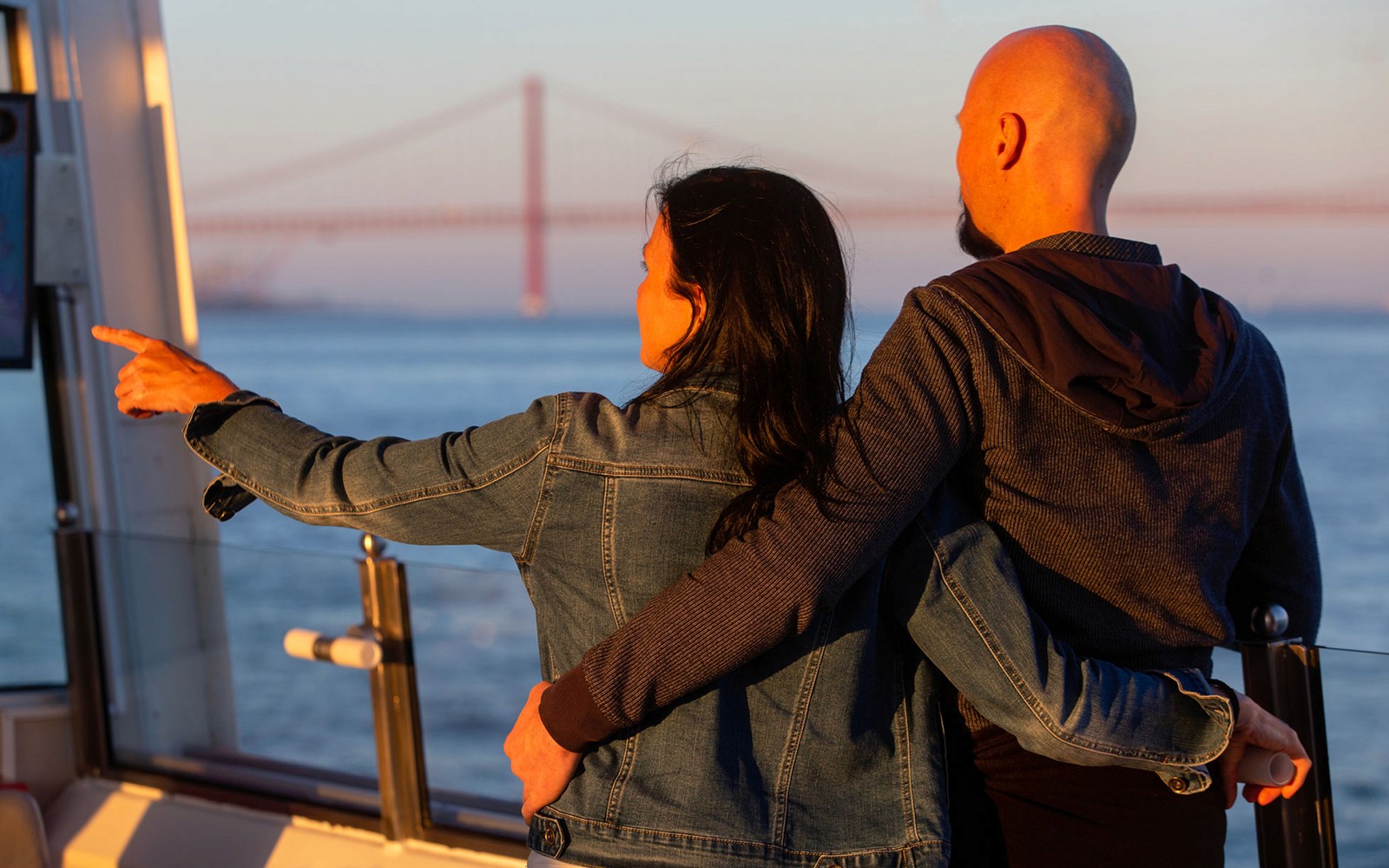 Couple enjoying sunset view of bridge on Tagus River cruise.
