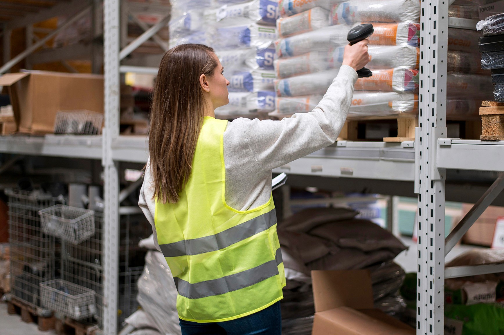 Woman in a yellow vest scans boxes with a barcode reader in a warehouse, inventory management.