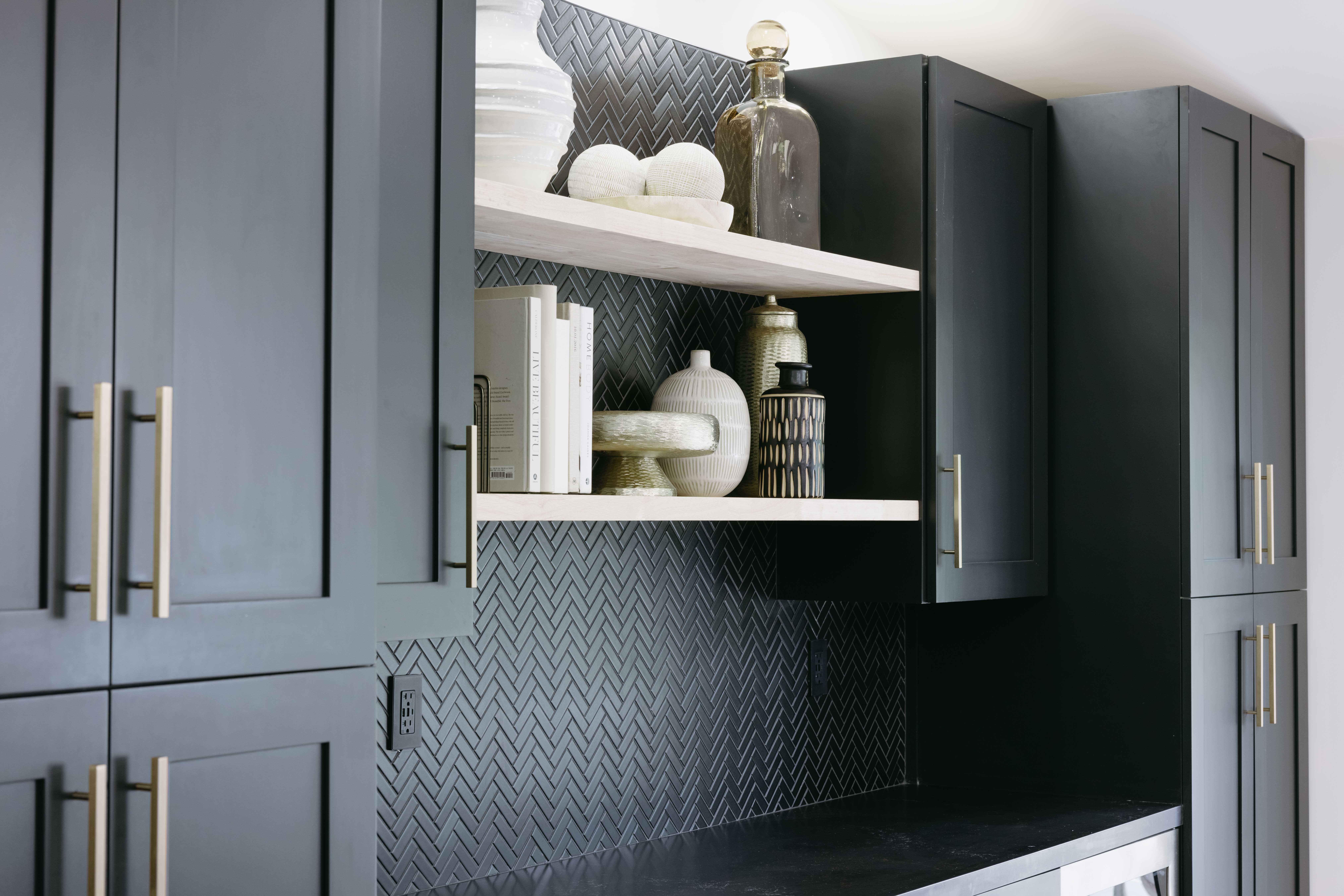 Modern dark gray kitchen cabinets with gold hardware and decorative items on shelves.
