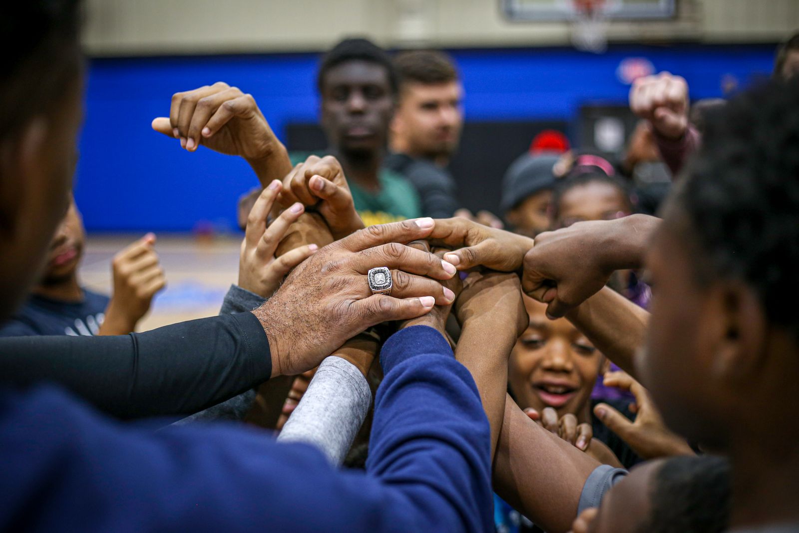 A group of kids and coaches join hands in a team huddle, symbolizing unity and teamwork during a basketball program.