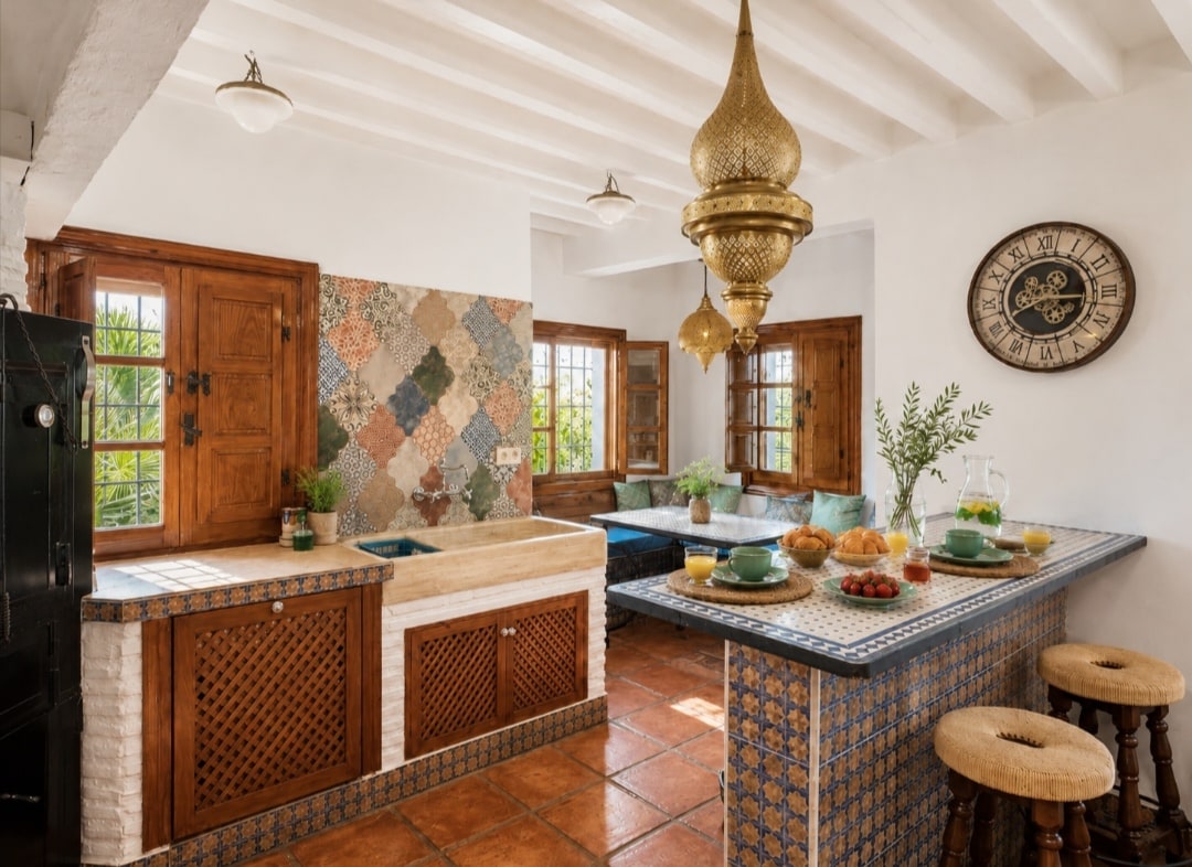 Cocina equipada con azulejos de colores, vigas y lámparas de latón