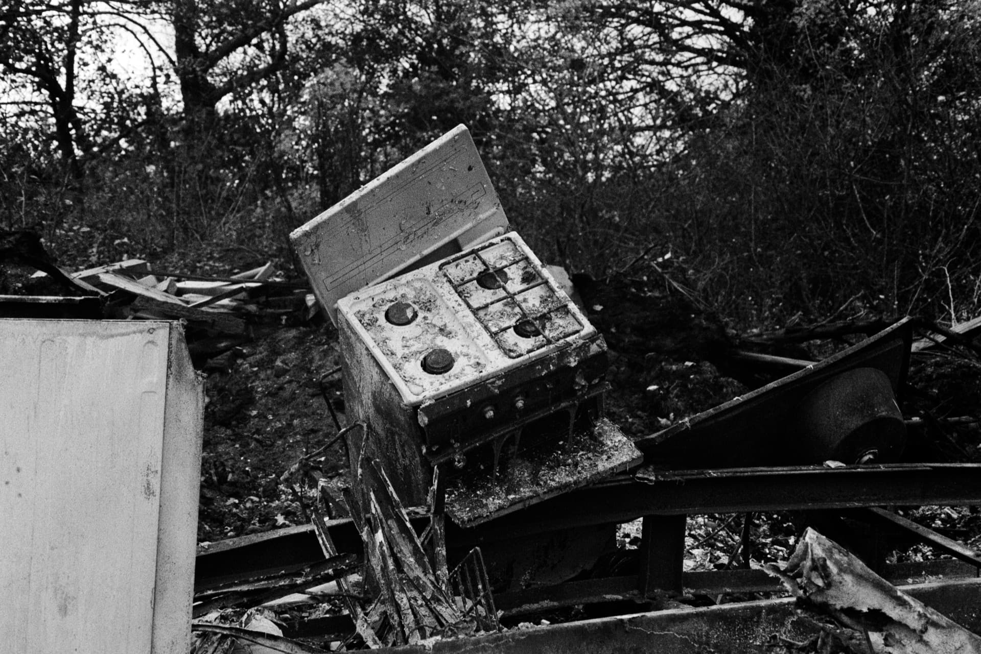 Weathered gas cooker discarded in woodland debris and fly-tipped waste