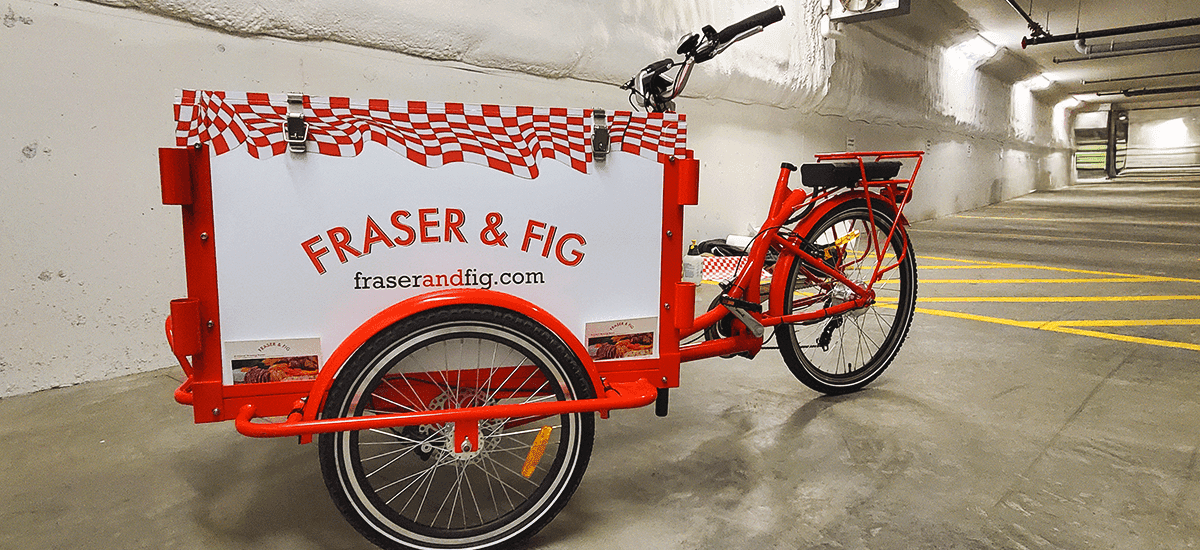 a red-and-white bicycle with fridge box attachment and vinyl wrap on top, reading Fig & Fraser on the sides and front