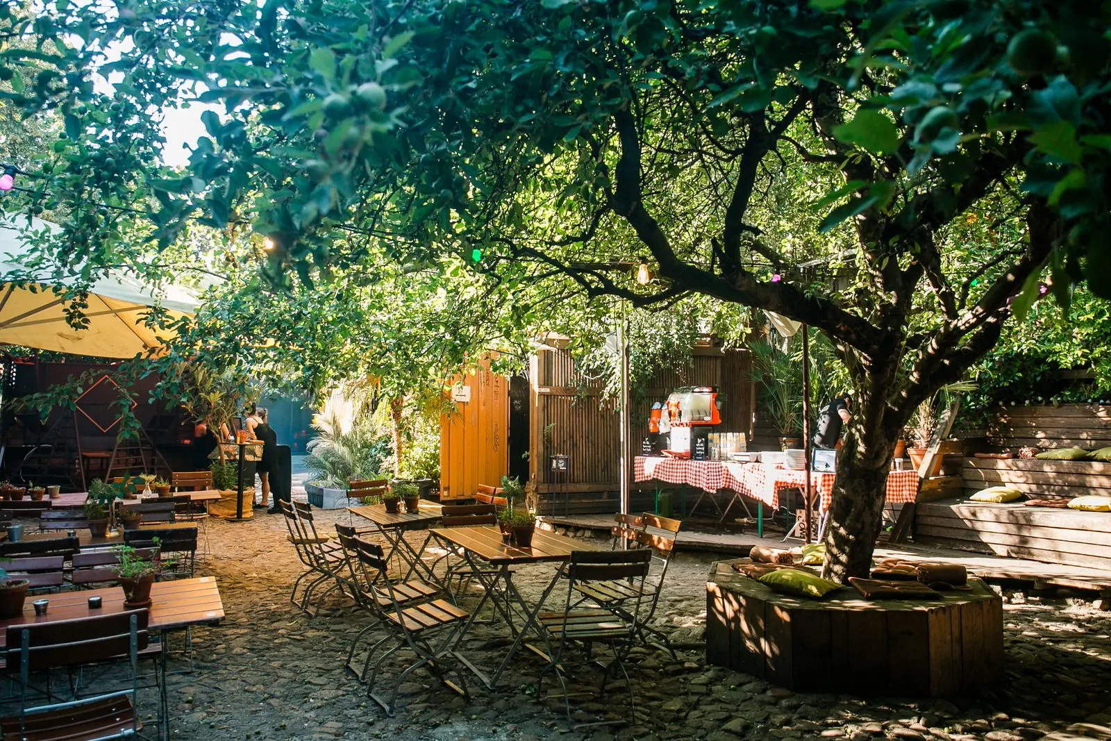 Garten unter einem großen Baum mit Tischen in der Oase Kreuzberg