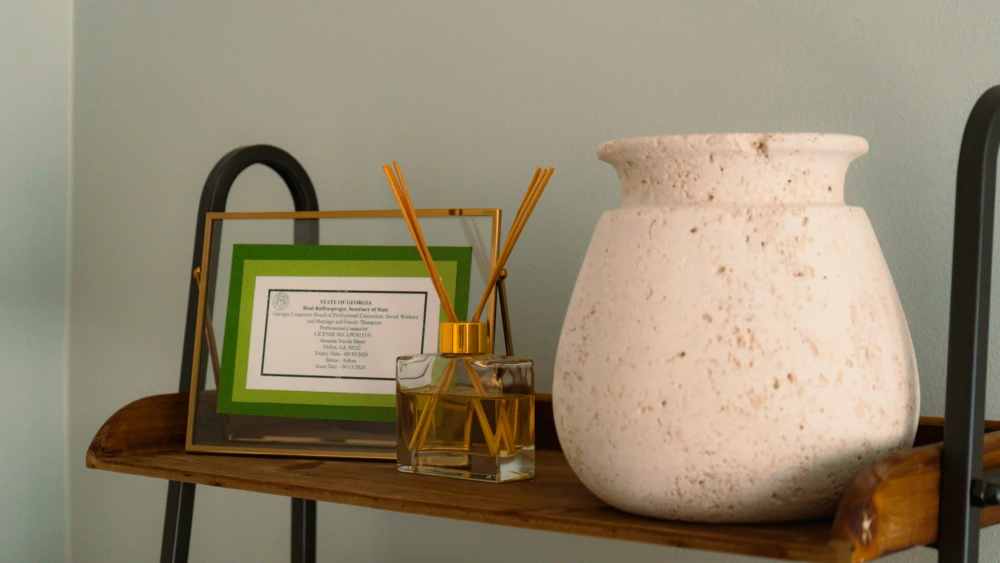 Wooden side table with diffuser, framed card, and ceramic vase.