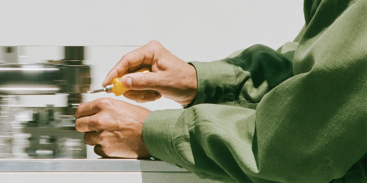 Person in green workwear using a screwdriver on a metal machine.
