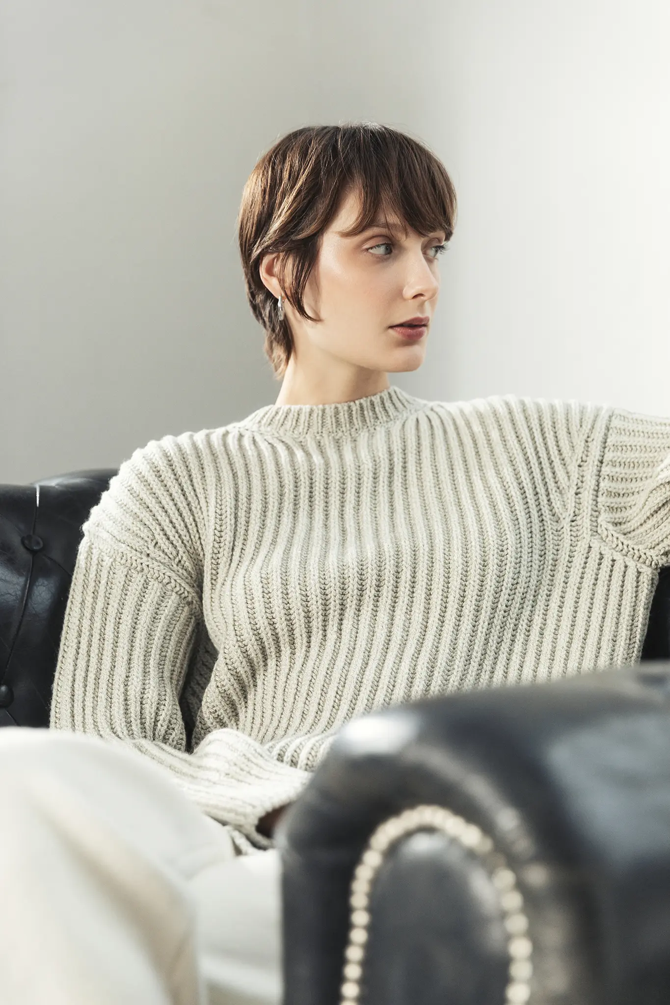 Woman sitting on leather armchair wearing beige ribbed cashmere sweater – Aida Barni FW25/26 collection.