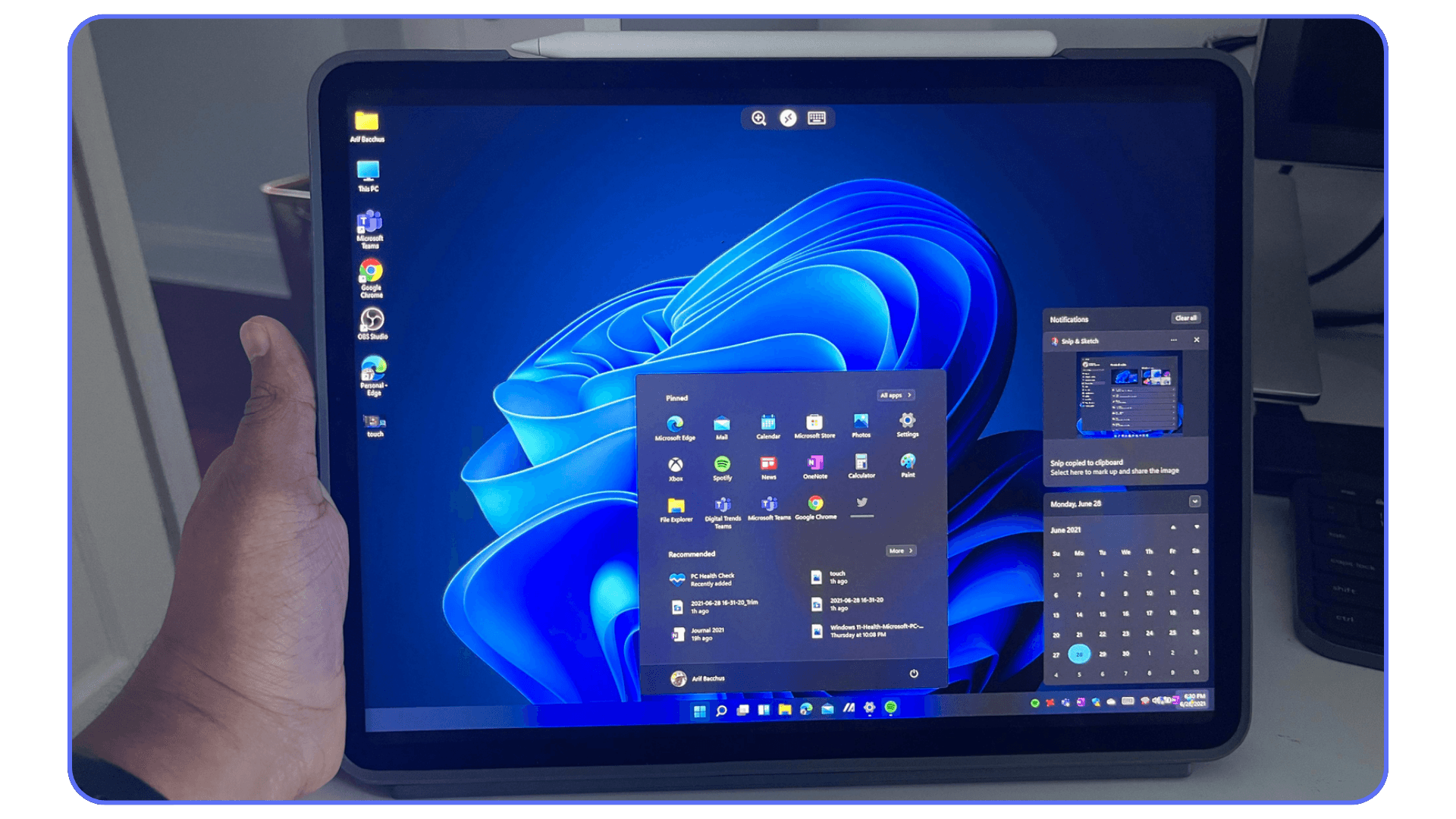 iPad displaying the Windows 11 interface, held in a hand with the Start menu open on screen.