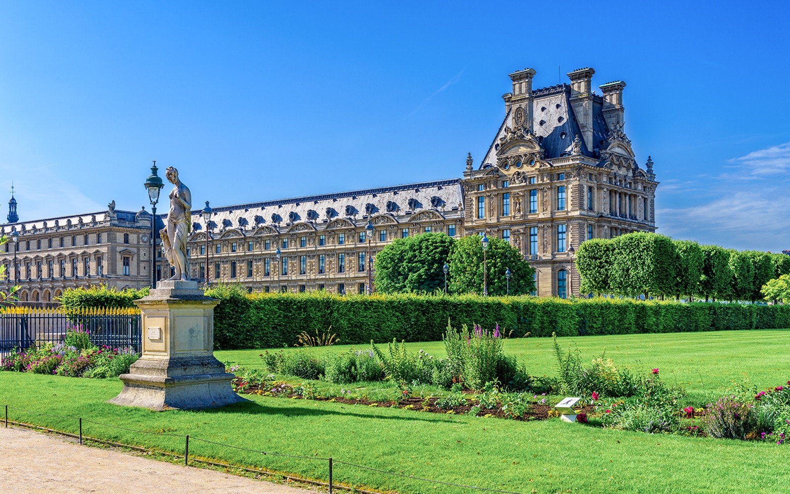 Louvre Museum with Tuileries Garden statue and manicured lawns in Paris.