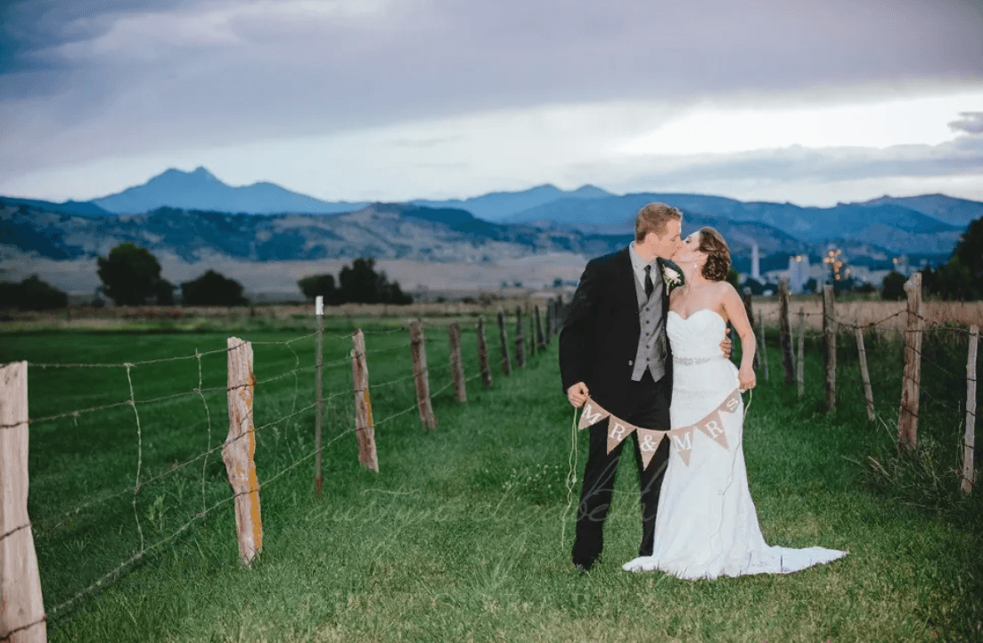 Bride and groom kissing at Shupe Homestead with mountain views in the background.