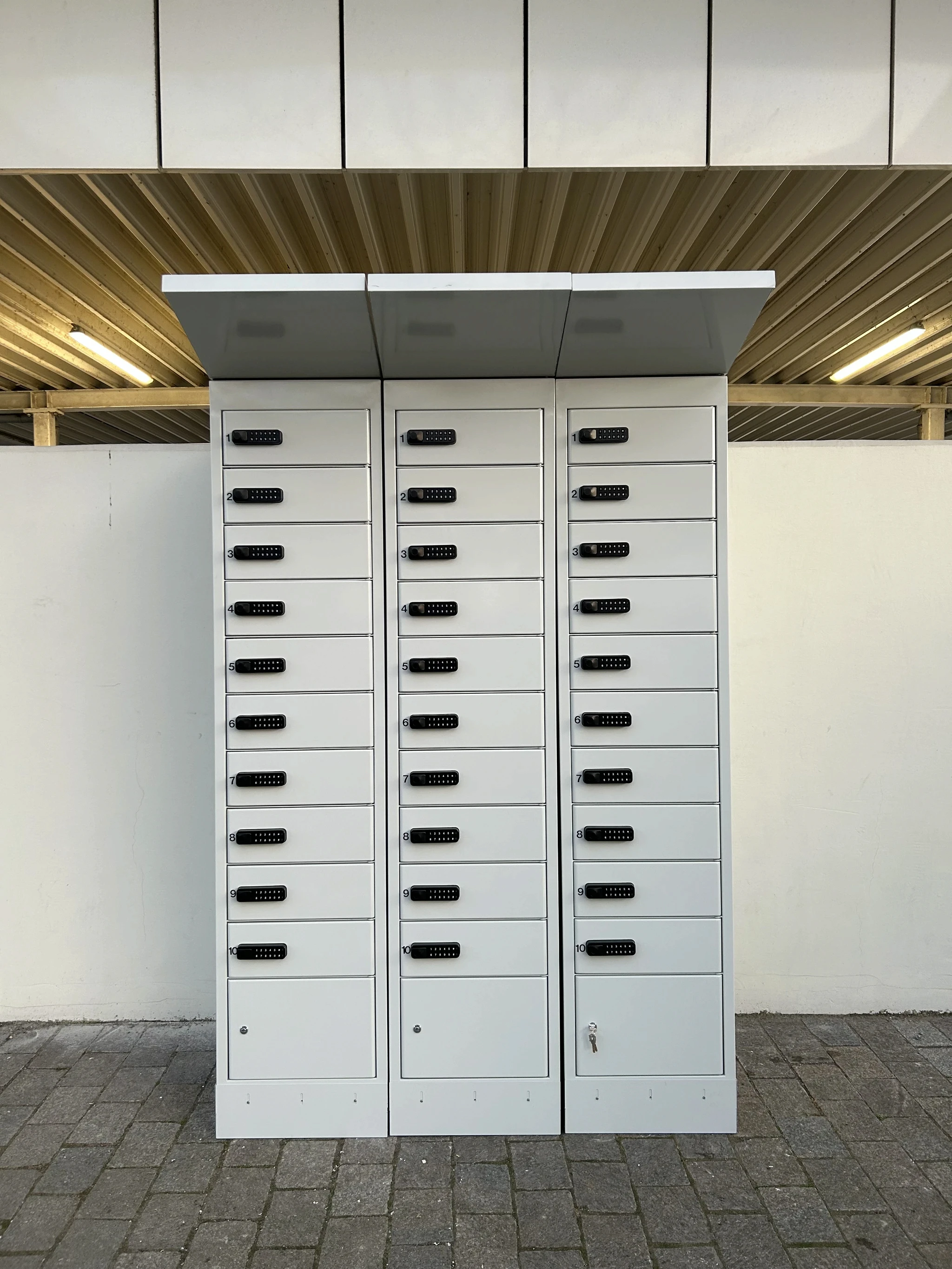 PowerShelter e-bike battery charging lockers installed outdoors, showing three units with numbered compartments and PIN locks.