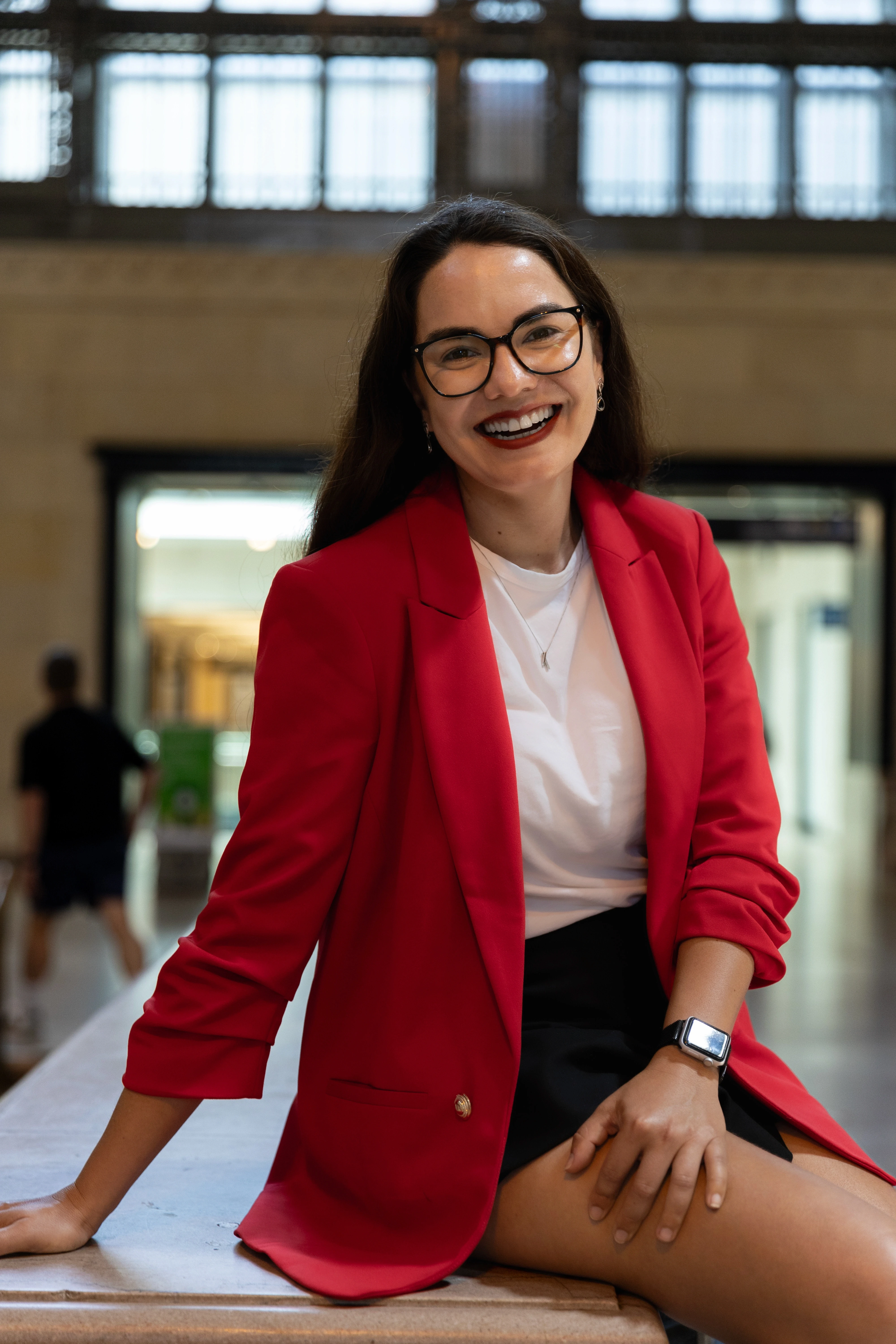 Mulher sorrindo de blazer vermelho em local interno de Toronto, em clima de boas-vindas.