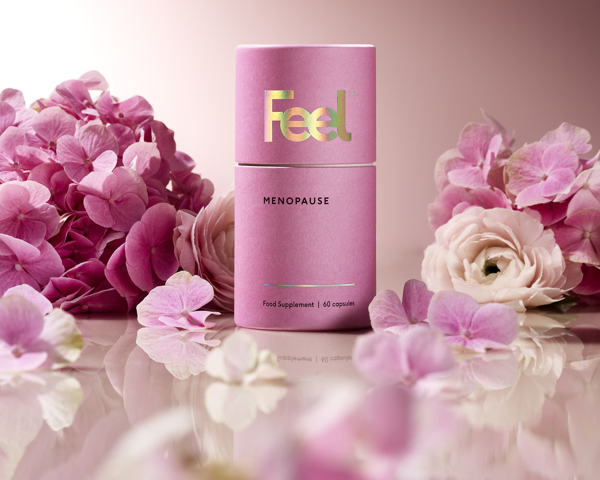 A pink skincare product is surrounded by soft pink flowers and petals on a light background.