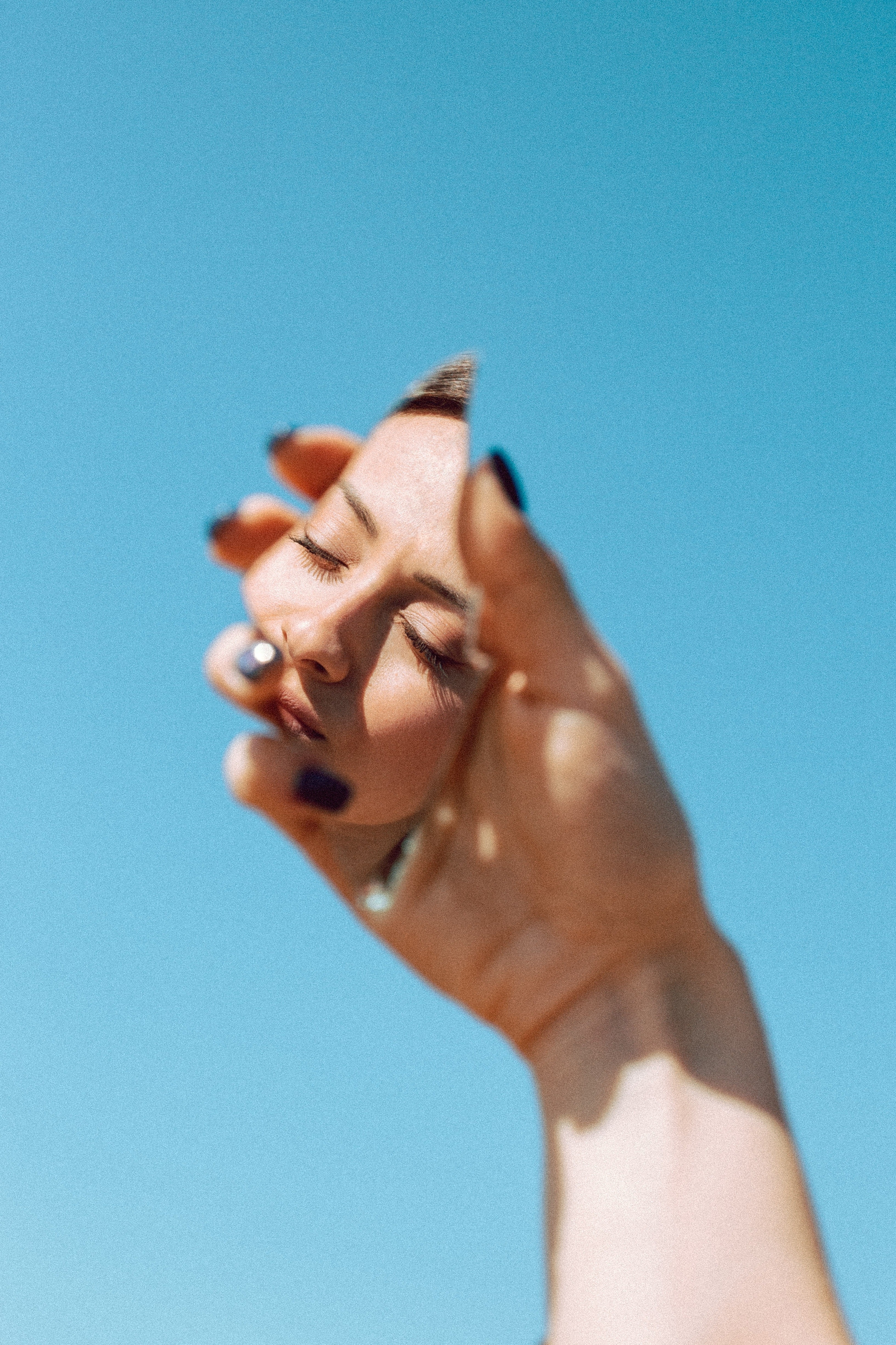 Hand holding a piece of broken mirror reflecting a woman's image, with the blue sky in the background.