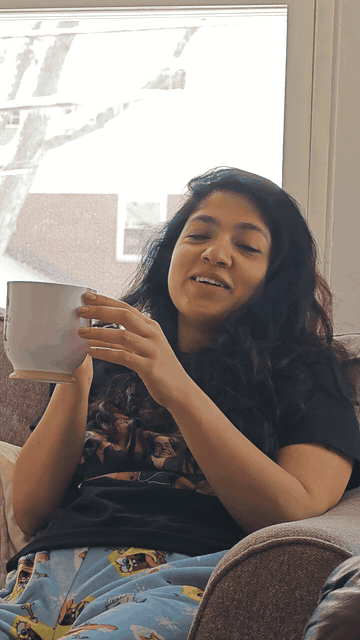 Sarika laughs with a mug beside a window overlooking snowy Albany