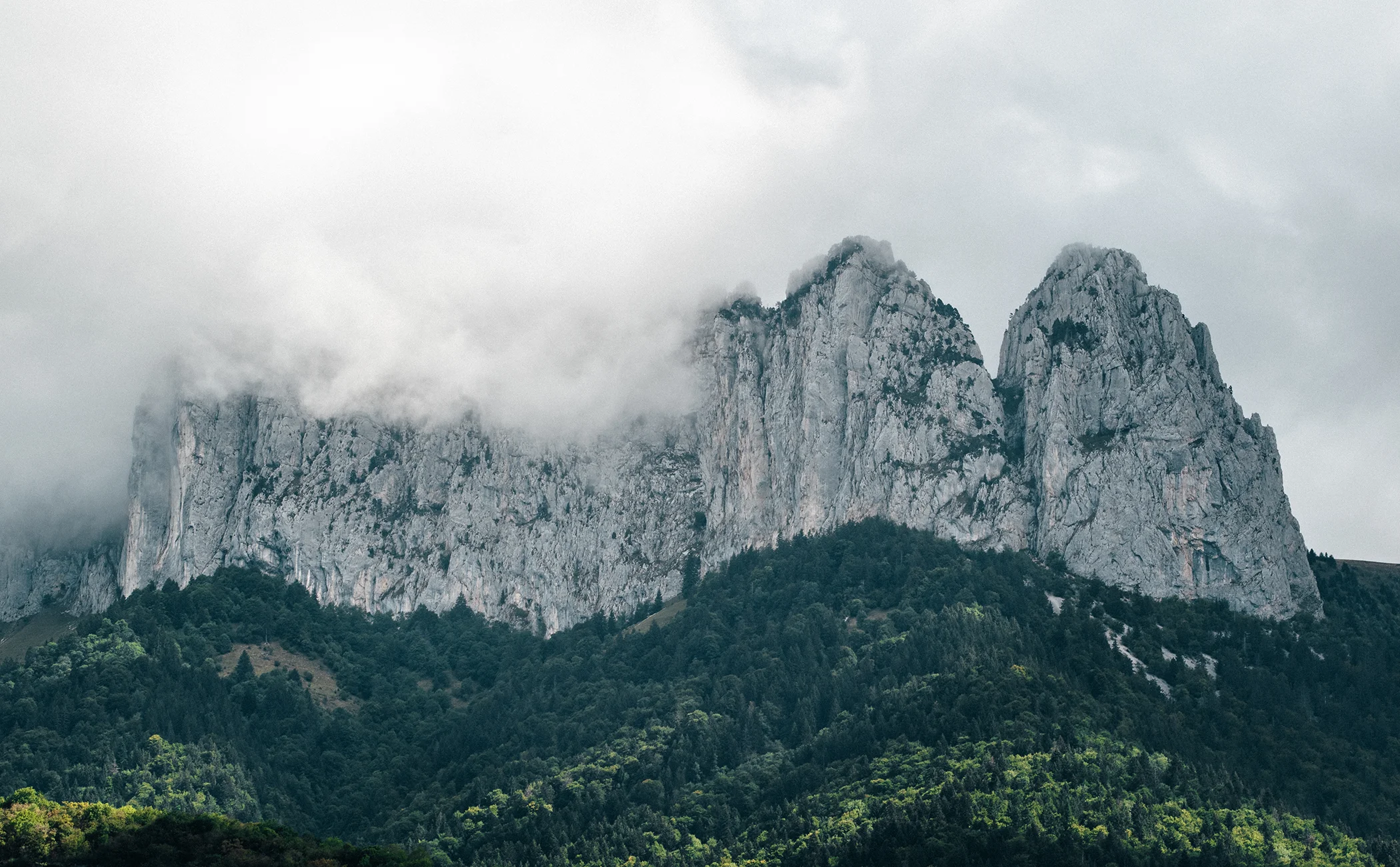 Des montagnes rocheuses émergent d’une forêt sous un ciel nuageux.