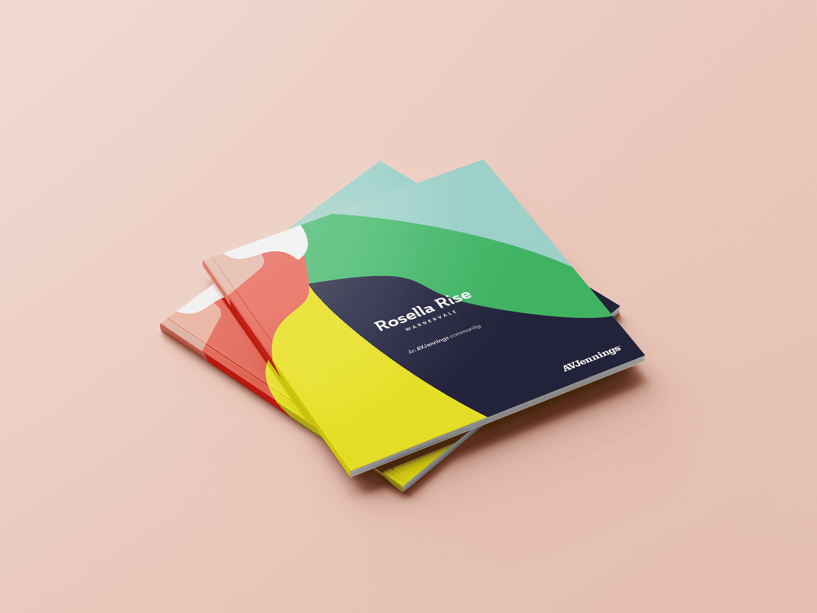 Three colourful books are stacked on a pale pink surface. The top book features vibrant abstract designs in yellow, green, and blue tones, with text on the cover.