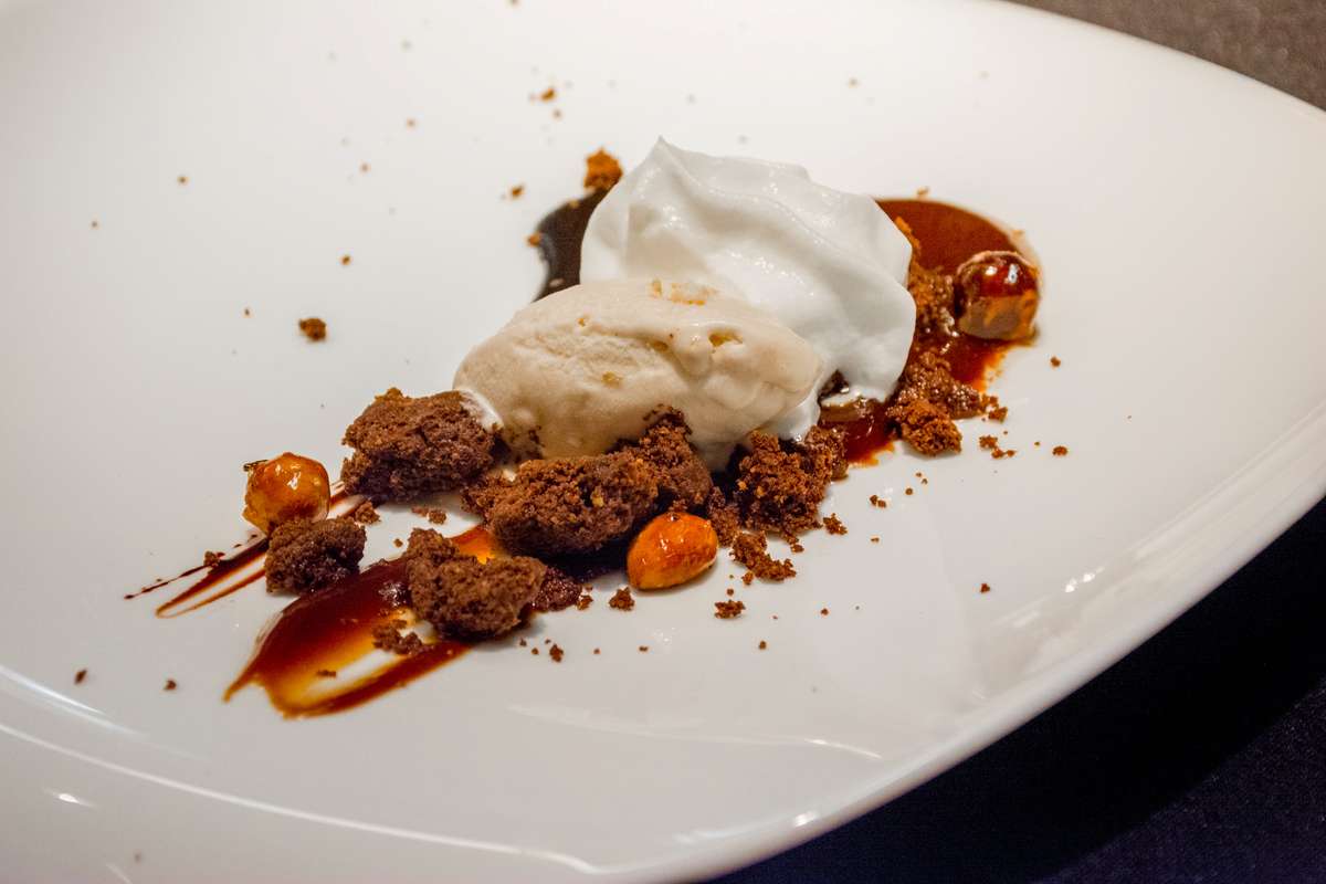 A plated dessert featuring a scoop of vanilla ice cream and a dollop of whipped cream with chocolate crumble and fruit.