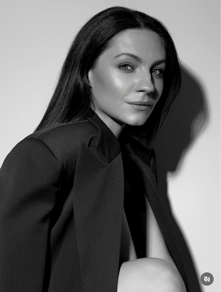 Black-and-white portrait of a man with an afro in motion, wearing a hoop earring and chain necklace, against a light gray background.