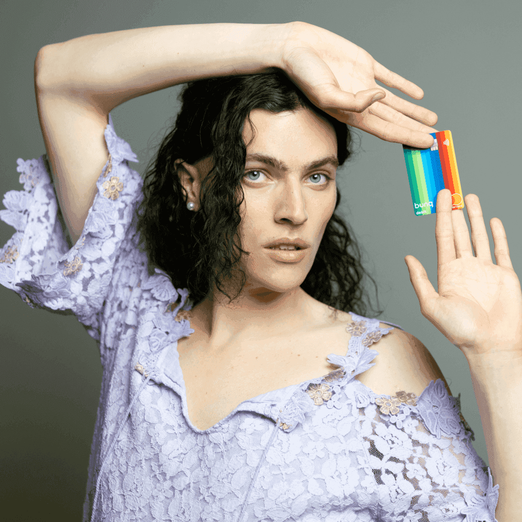 Een persoon met golvend haar poseert dramatisch en houdt kleurrijke objecten bij hun gezicht tegen een neutrale achtergrond.