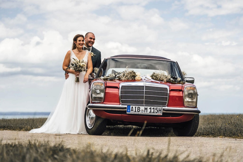 Brautpaar vor rotem Oldtimer auf Feld bei Hochzeit am Chiemsee