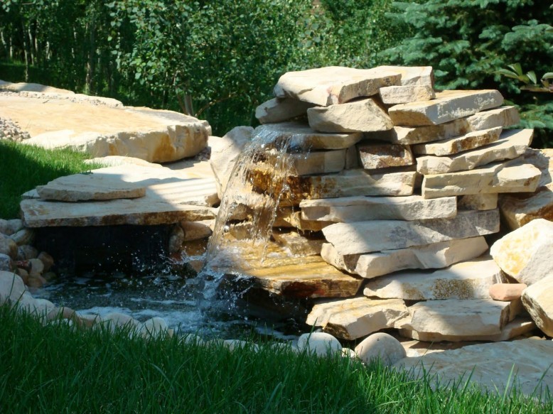 large natural stones stacked to create an outdoor waterfall feature in a backyard