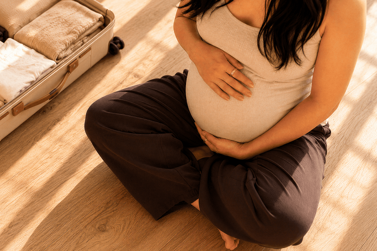 Pregnant person cradling their belly next to her open suitcase