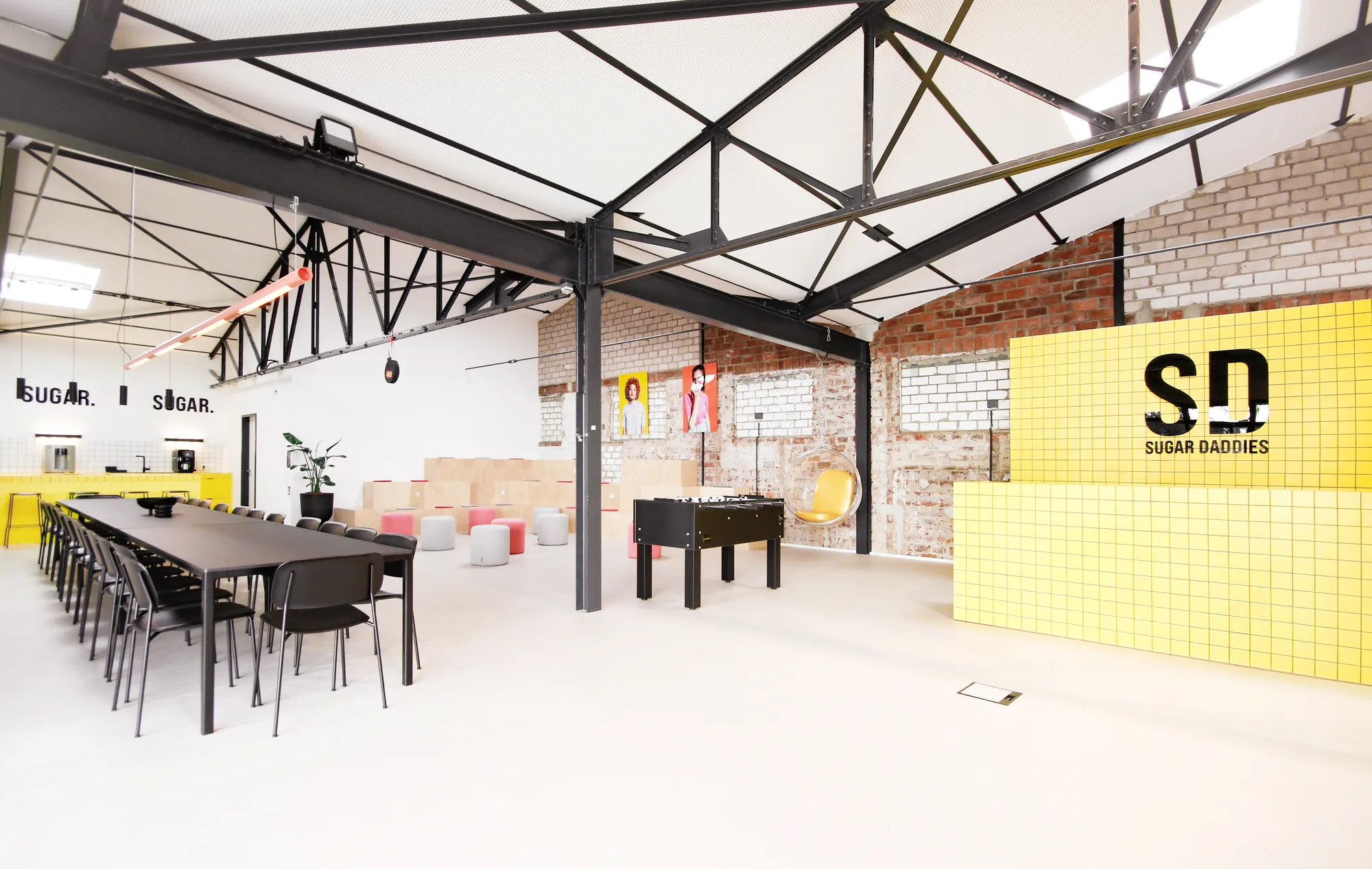 Loft overview with long dining table, foosball, yellow SD counter and SUGAR lettering.