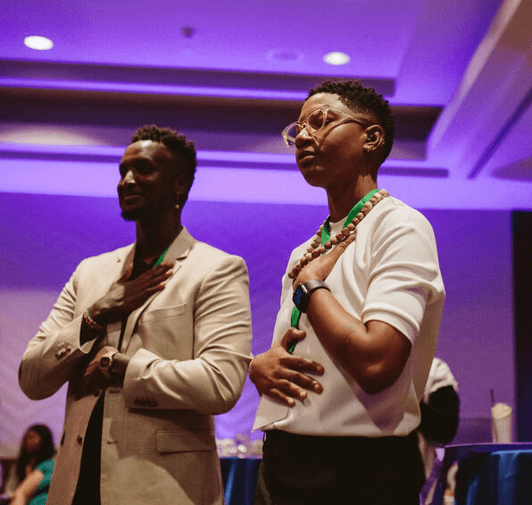 Three individuals stand in a dimly lit room with purple lighting, engaged in conversation or listening intently.
