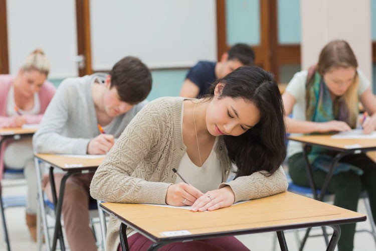 High school students, including focused young women and men, writing in a classroom during RISE Research and STEM summer programs or academic tests.