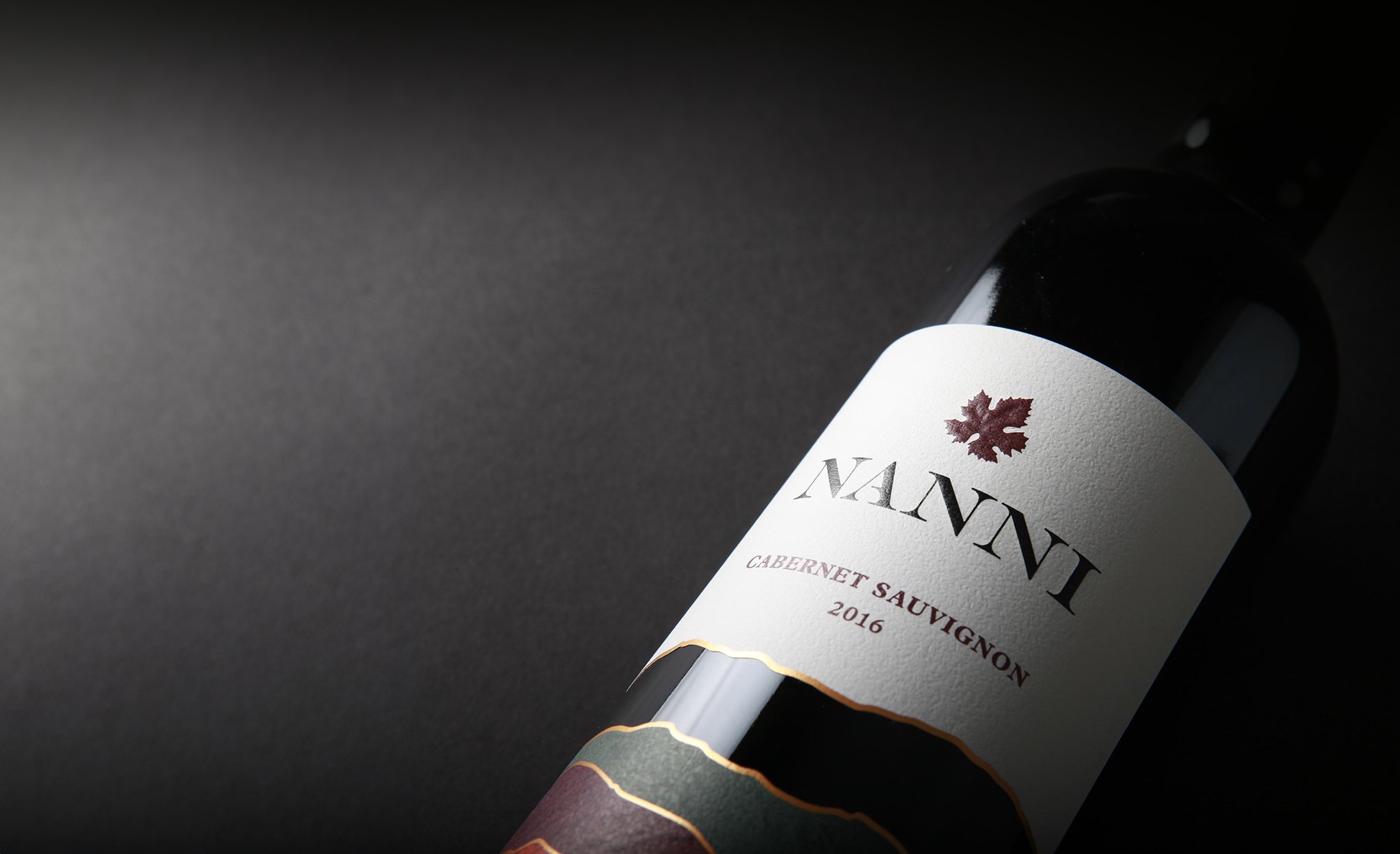 A wine bottle labeled "Nanni Cabernet Sauvignon 2016" is angled on a dark background, emphasizing elegance and sophistication with warm highlights.