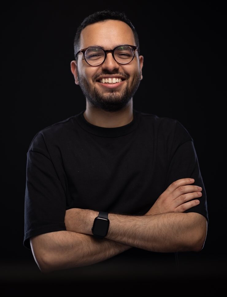 Portrait of a young man with short hair, wearing a dark t-shirt, against a plain background.