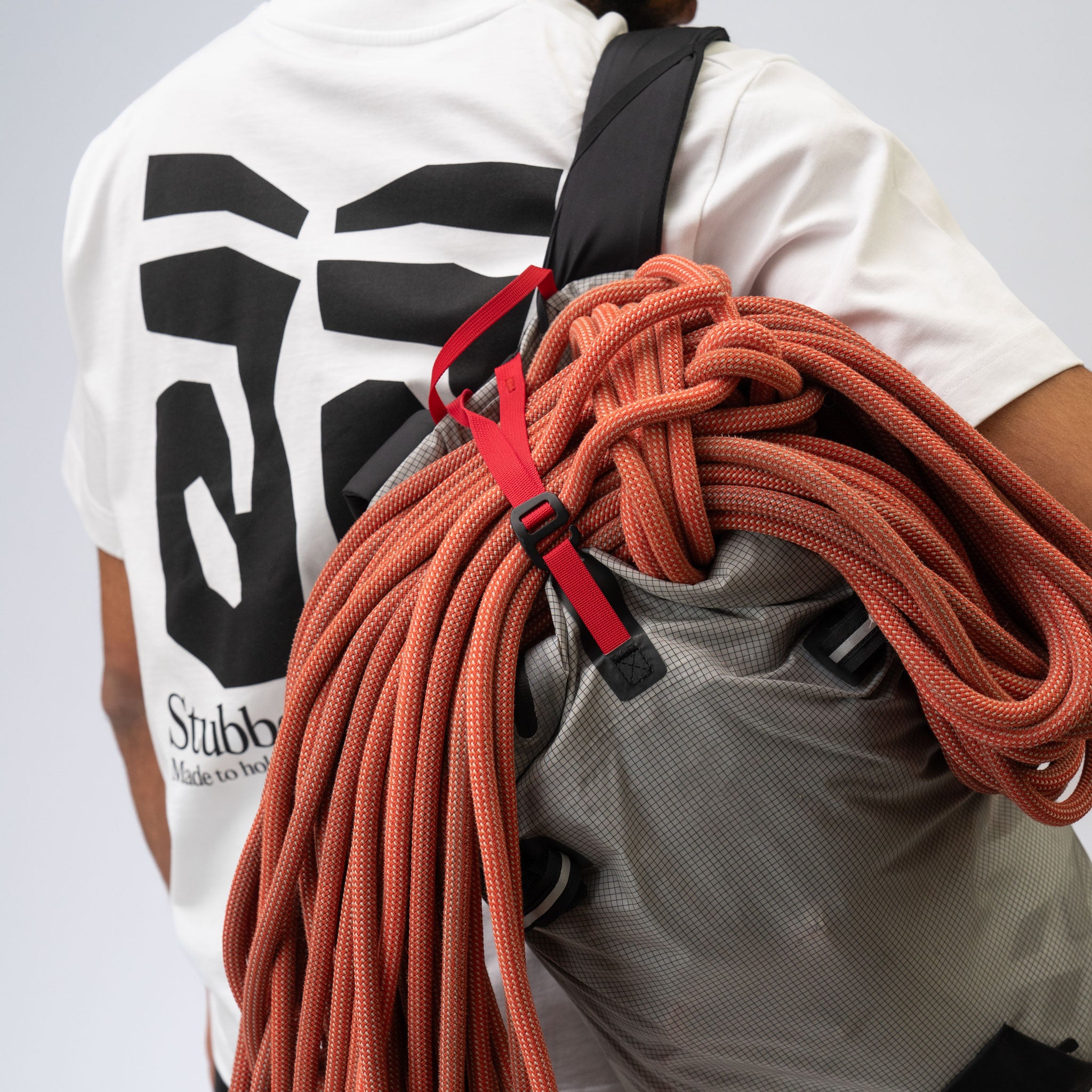 Person wearing a white shirt with black text and a backpack filled with orange climbing rope.