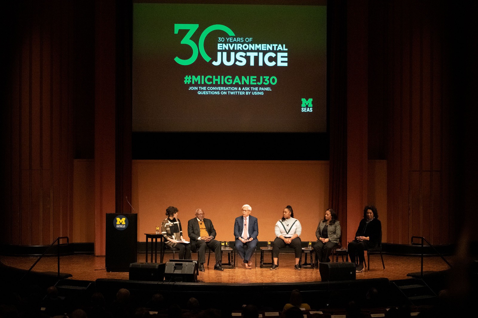 Panel discussion on stage with a large screen displaying the "30 Years" logo, in an auditorium setting.