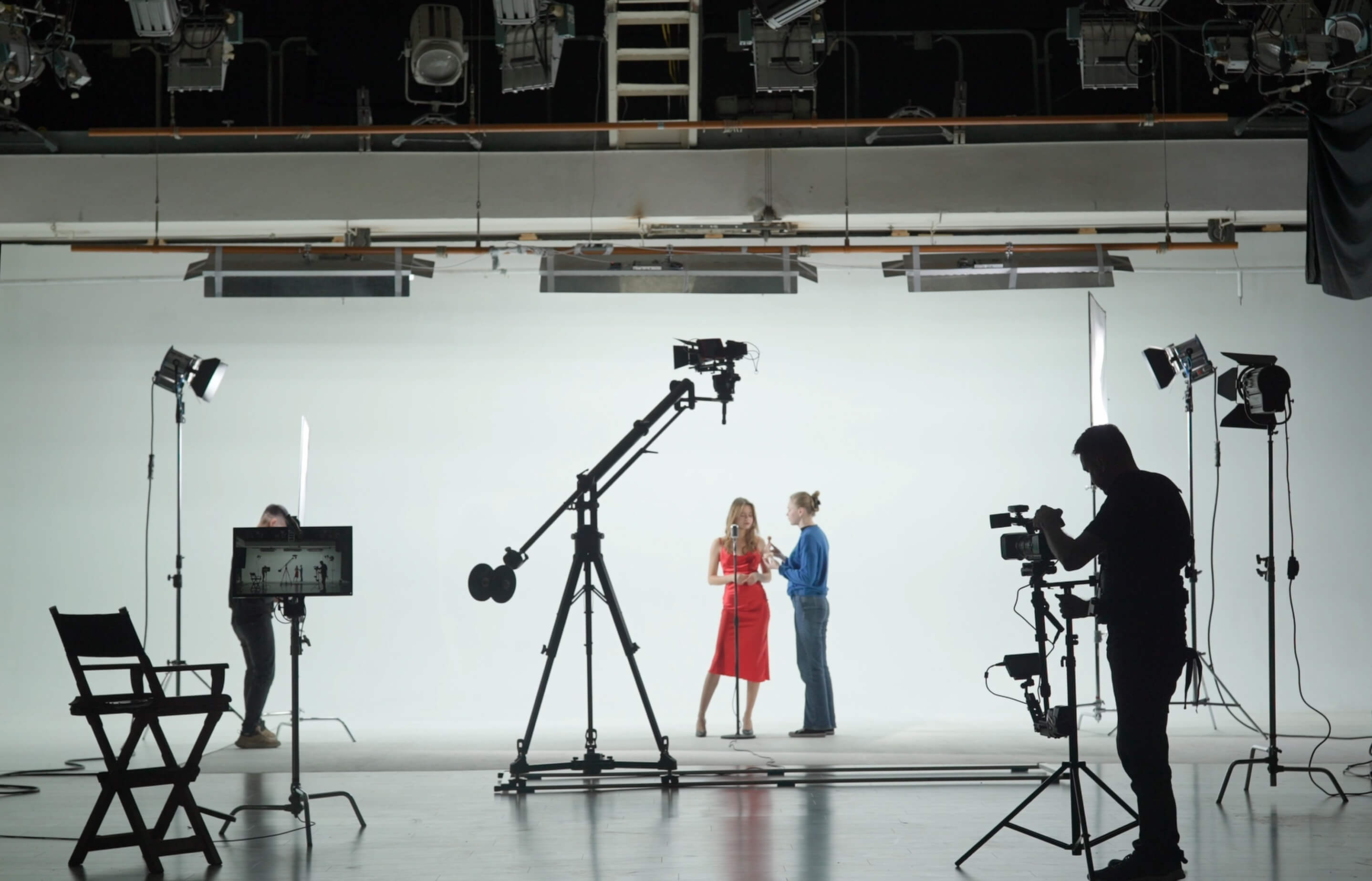 A photographer captures two models, one in a red dress, in a studio with multiple cameras and lights.