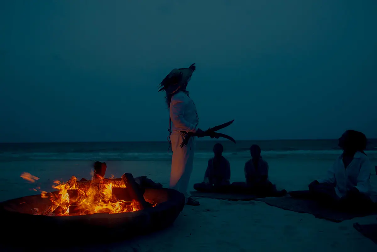 Grupo de personas alrededor de una fogata en una ceremonia maya al atardecer junto al mar en Nômade Tulum, México.