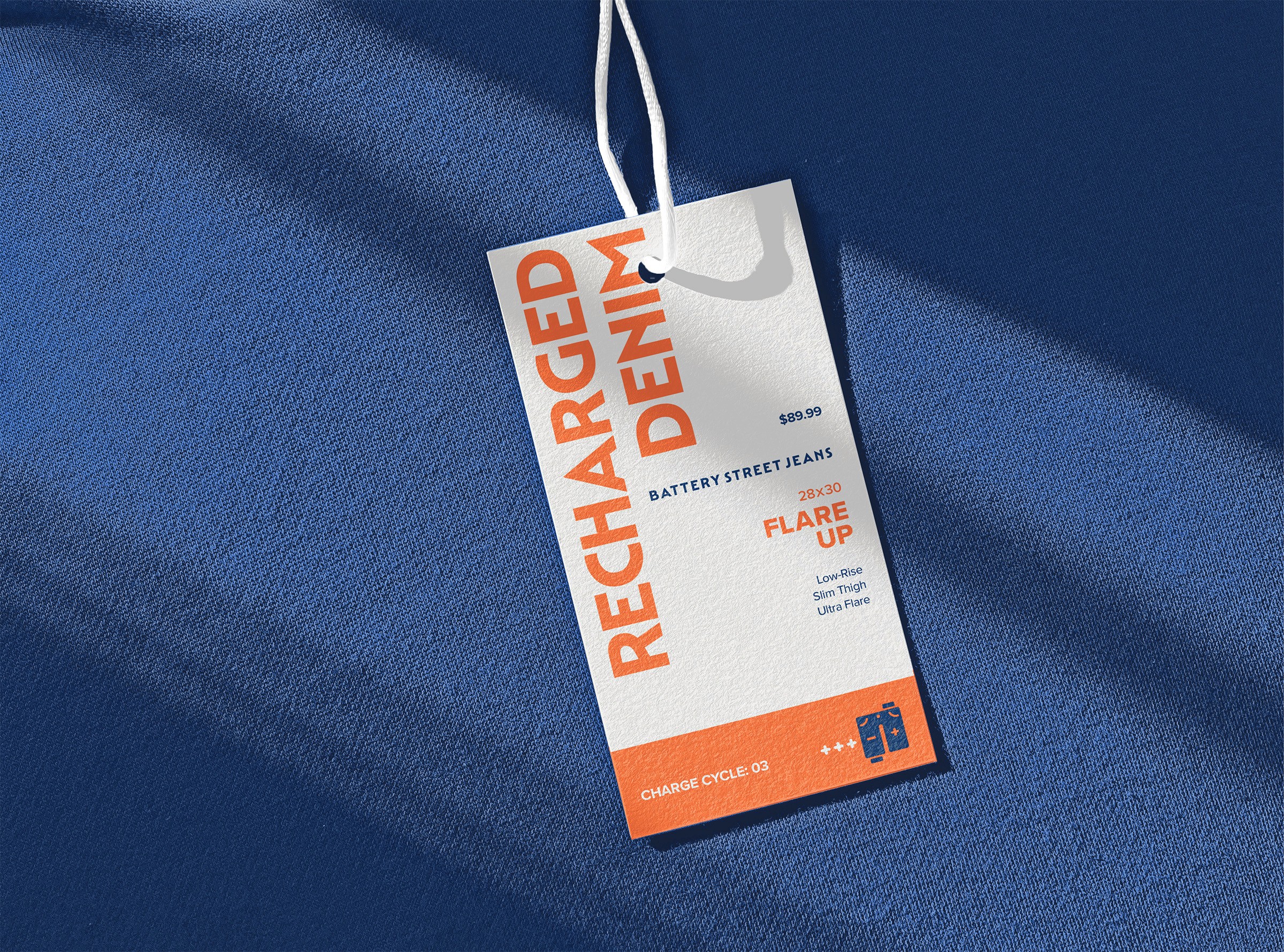 A white clothing tag labeled "Recharged Denim" with text and icons in orange and blue hangs by a string over a textured blue fabric surface, casting soft shadows.