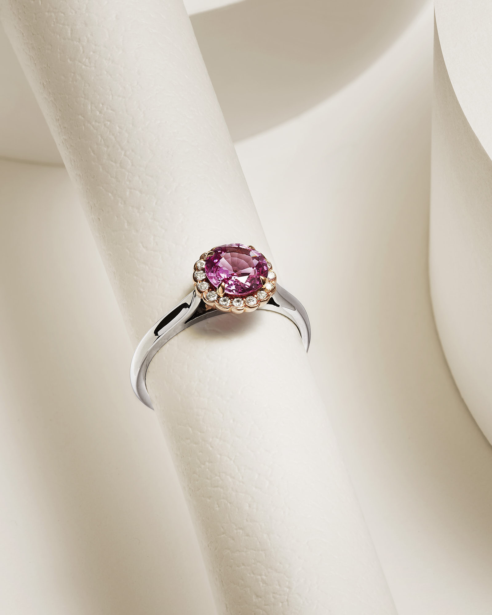 Elegant silver ring with pink gemstone and diamond accents on a textured white background.