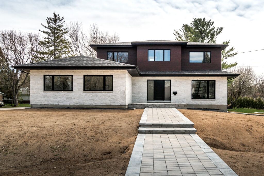 Modern two‑storey home with dark upper and light stone‑clad lower exterior, paved front walkway and large windows showcasing the high‑end residential properties serviced by B&Y Reno Corp