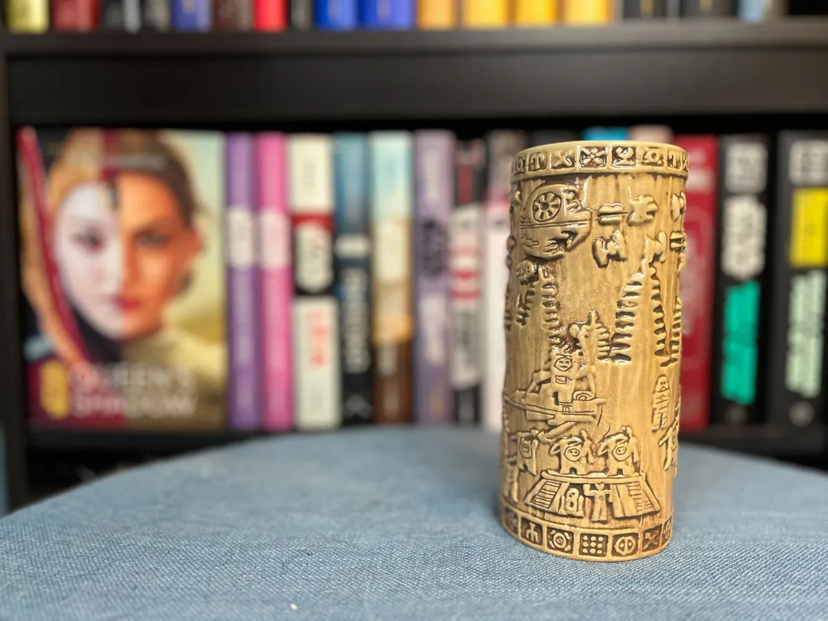 A mug from Oga's Cantina in Galaxy's Edge showing the Battle of Endor. The mug is on a blue surface with a blurred Star Wars bookcase in the background