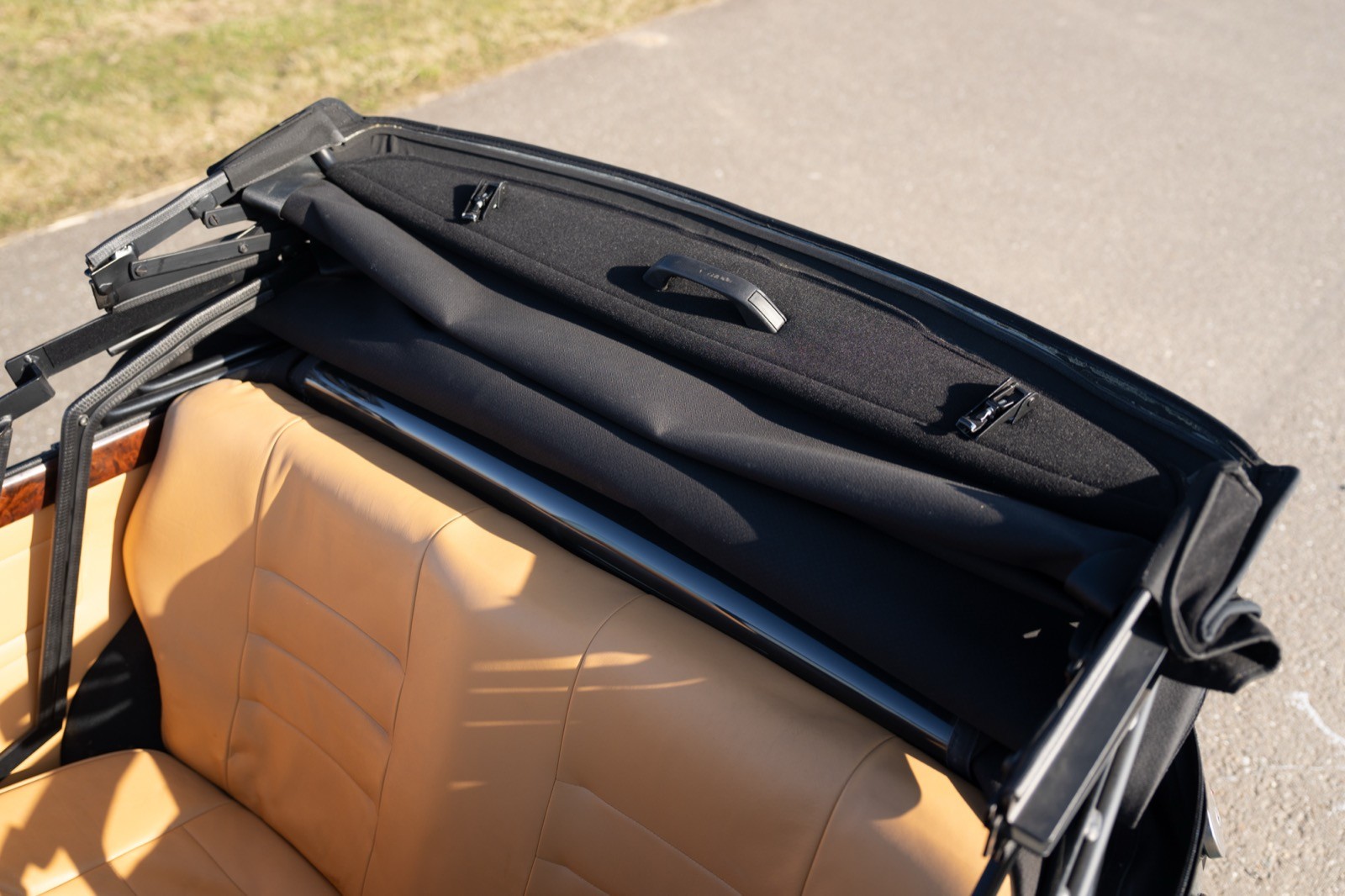 A close-up view of the rear deck and seat area of a convertible car, showcasing tan upholstery and a black trim.