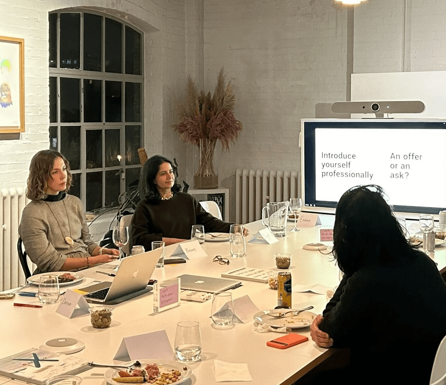 A group of four people engaged in a meeting around a table with a presentation on a screen.